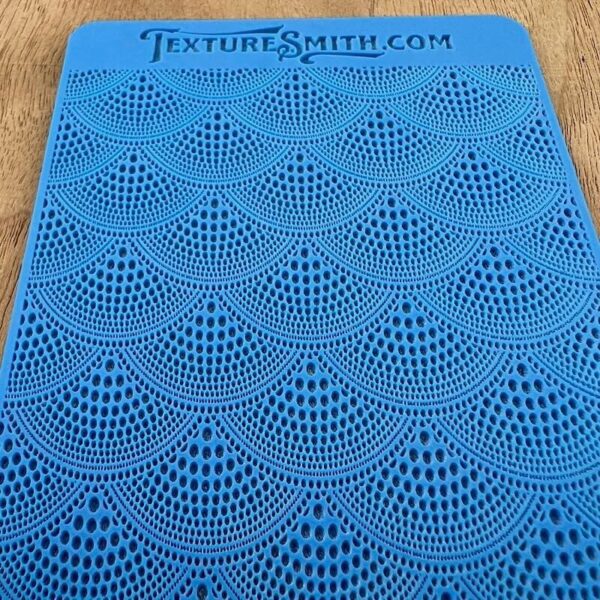 Blue fabric with intricate fan-shaped lace patterns.