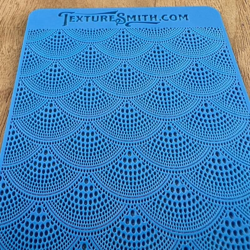 Blue fabric with intricate fan-shaped lace patterns.