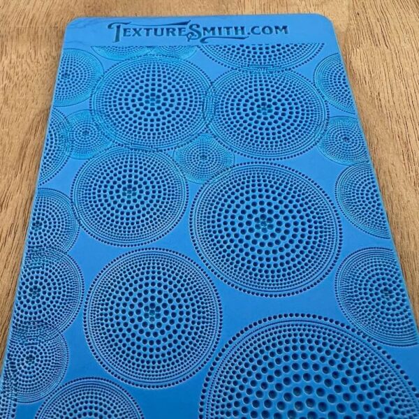 Blue stencil sheet with concentric circle patterns on a wooden surface.