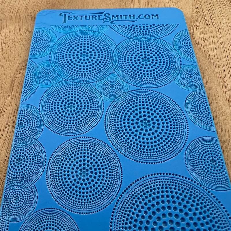 Blue stencil sheet with concentric circle patterns on a wooden surface.