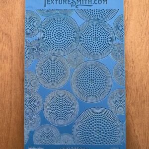 A blue stencil sheet with circular geometric patterns on a wooden surface.
