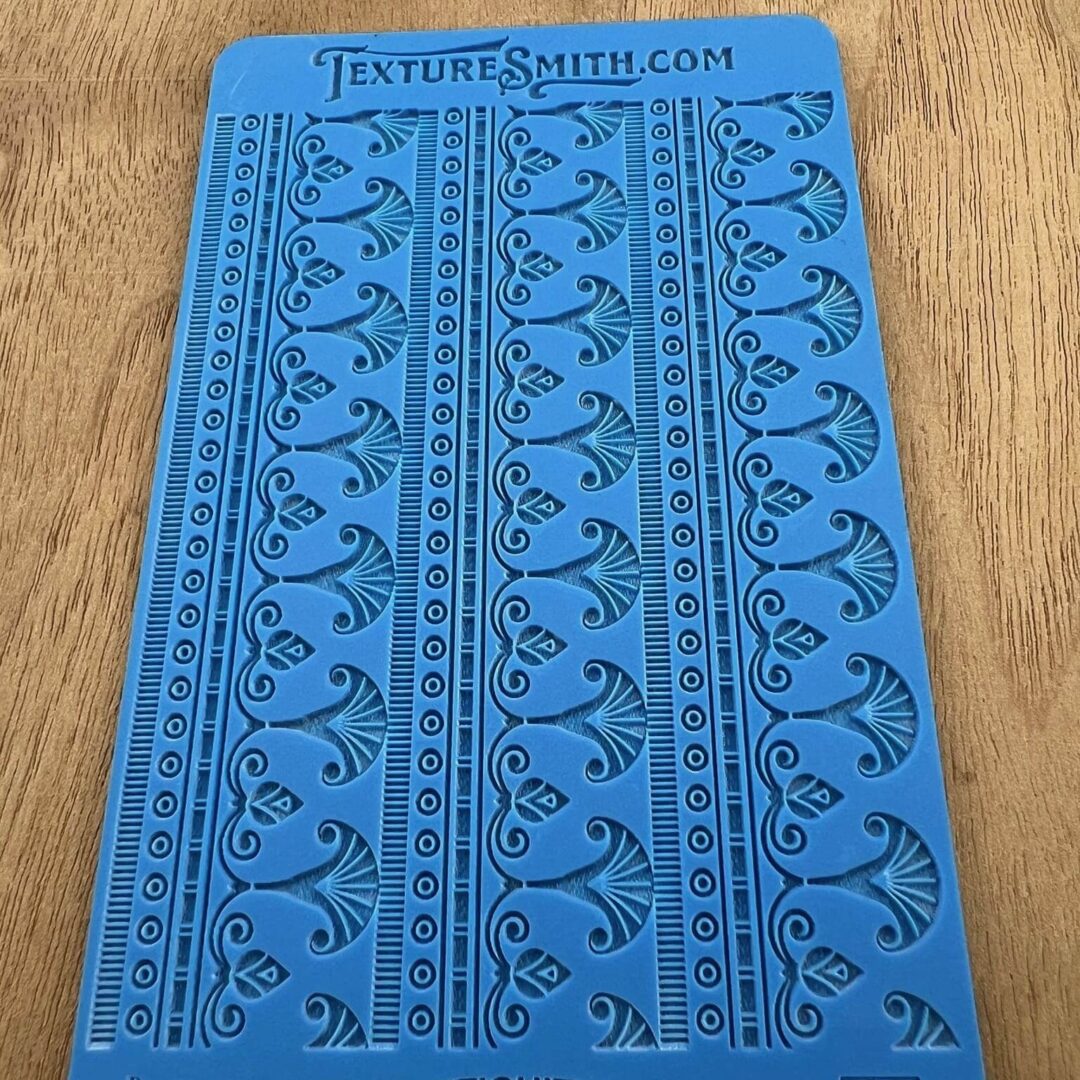 Blue stencil with floral and geometric patterns on a wooden surface.