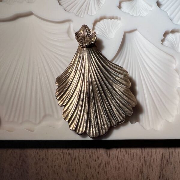 A silver shell-shaped pendant on a textured surface.