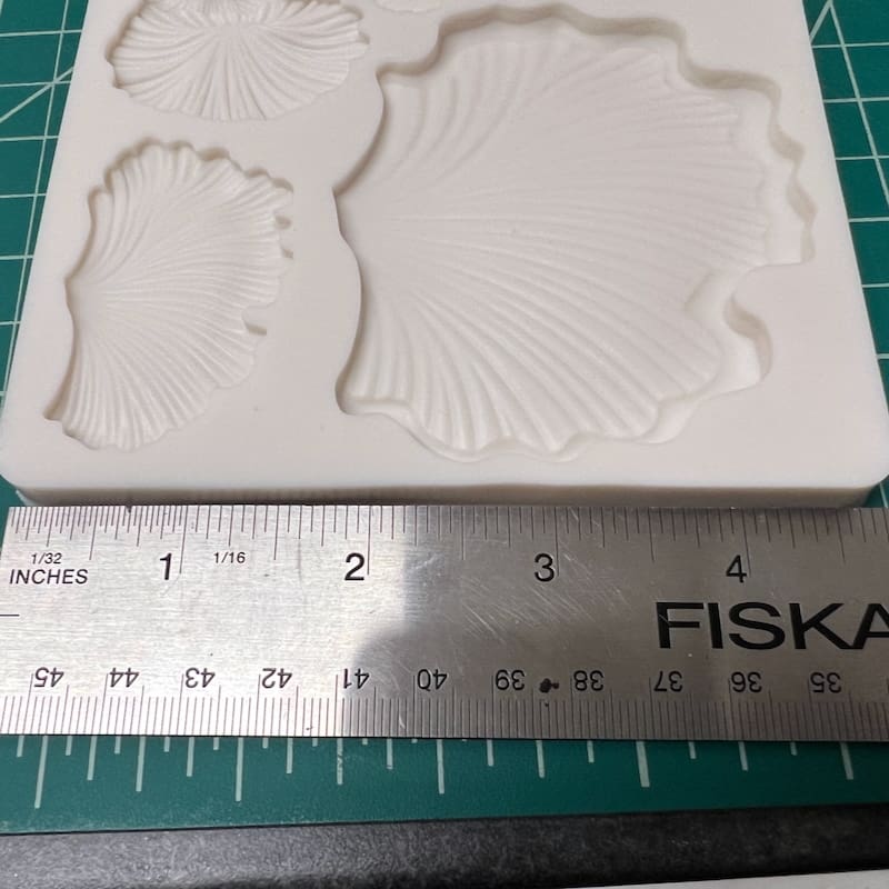 White silicone mold with seashell and footprint shapes beside a ruler.
