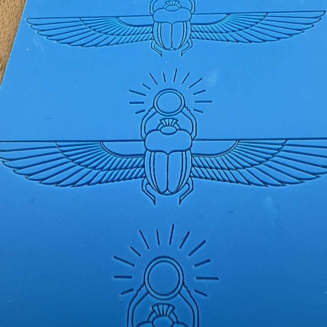 Three blue Egyptian scarab designs with wings and sun motifs.