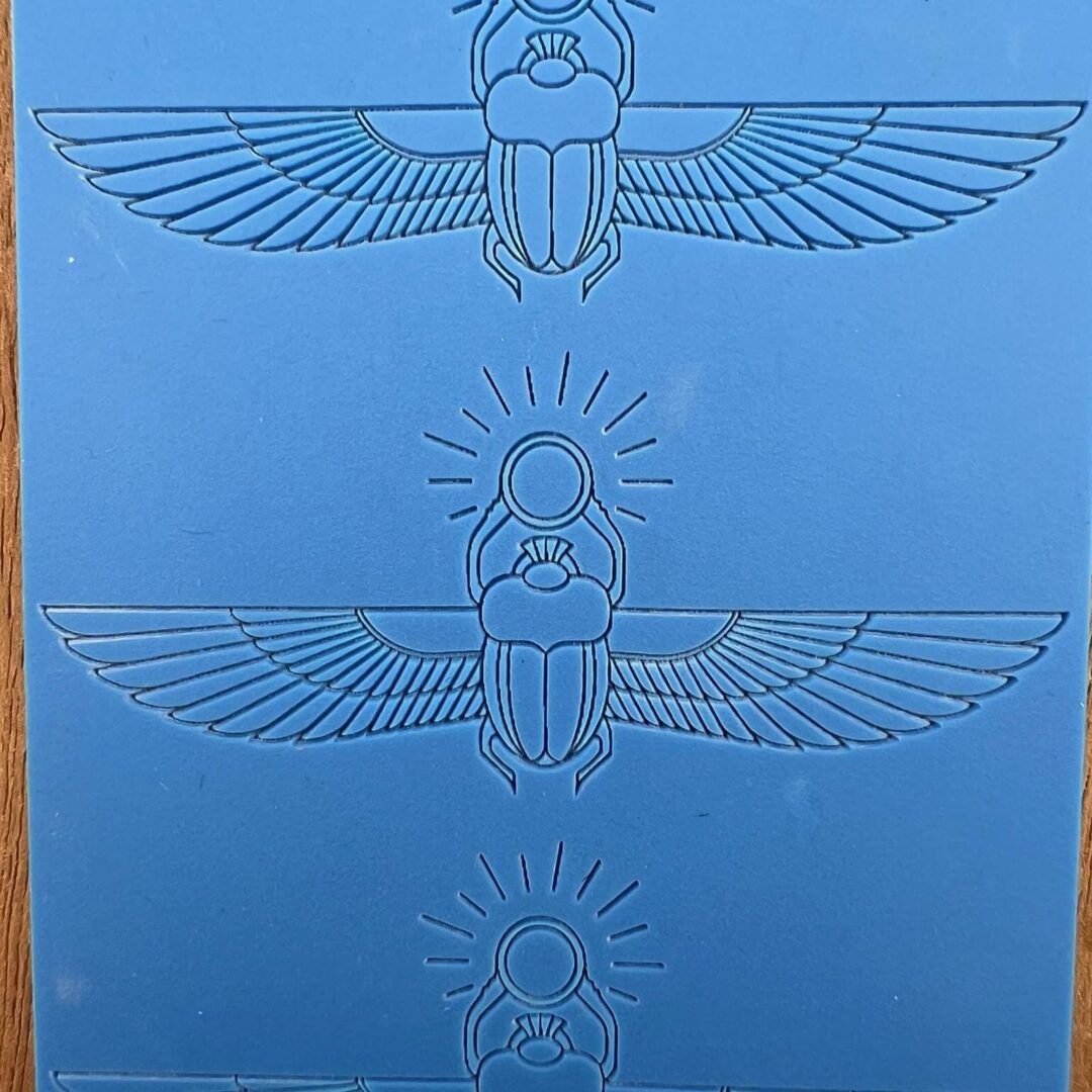Three blue embossed Egyptian scarab designs with wings on a blue background.