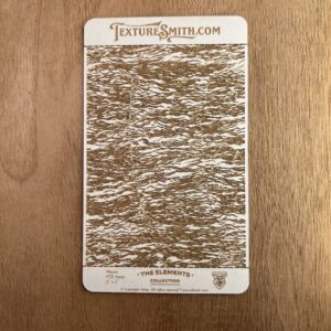 Vintage textured card with intricate brown and white pattern on wood surface.