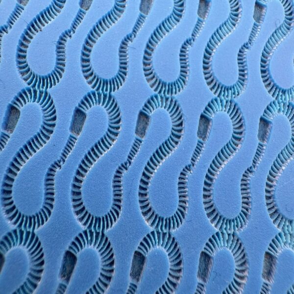 Close-up of a blue fabric with a repeating wavy cutout pattern.