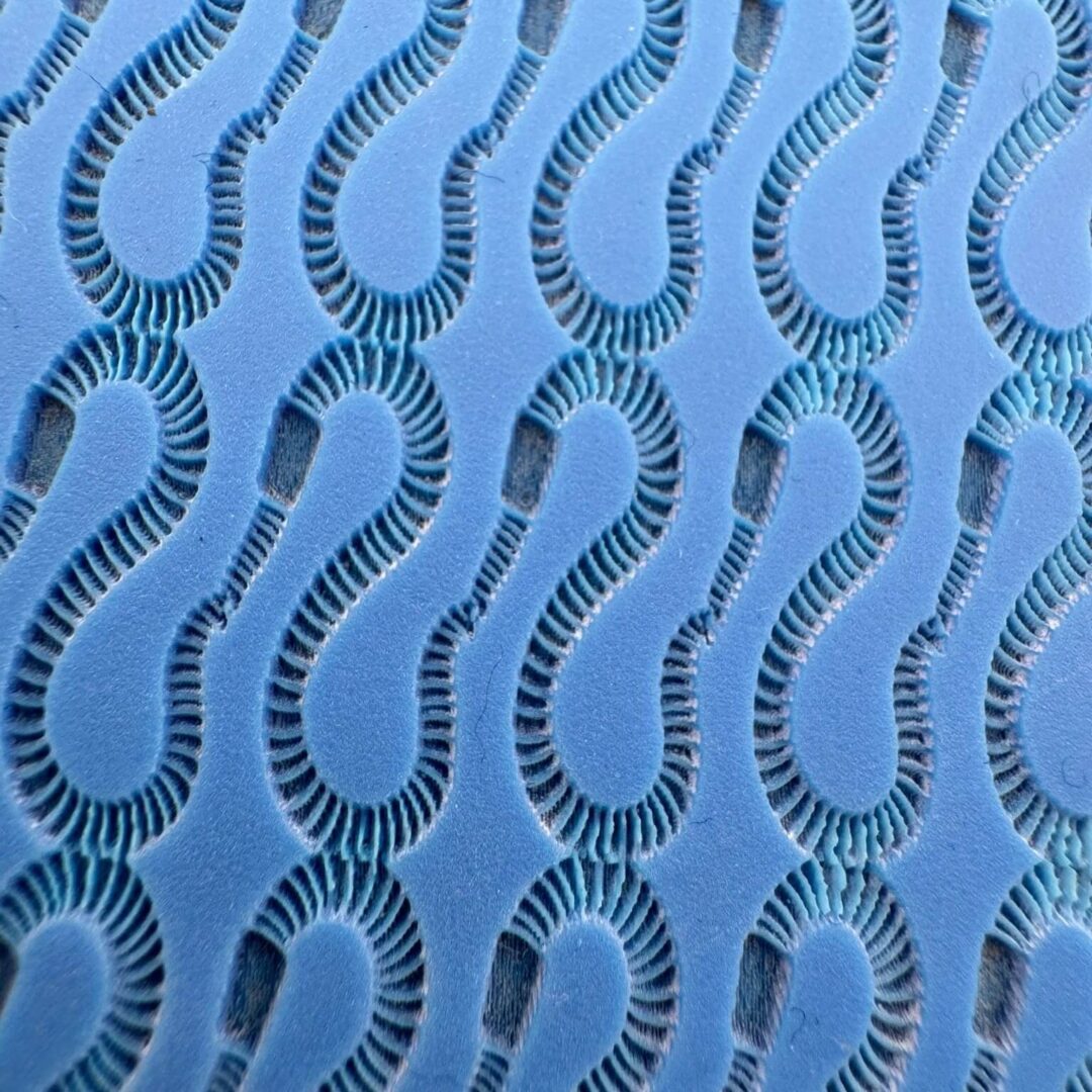 Close-up of a blue fabric with a repeating wavy cutout pattern.
