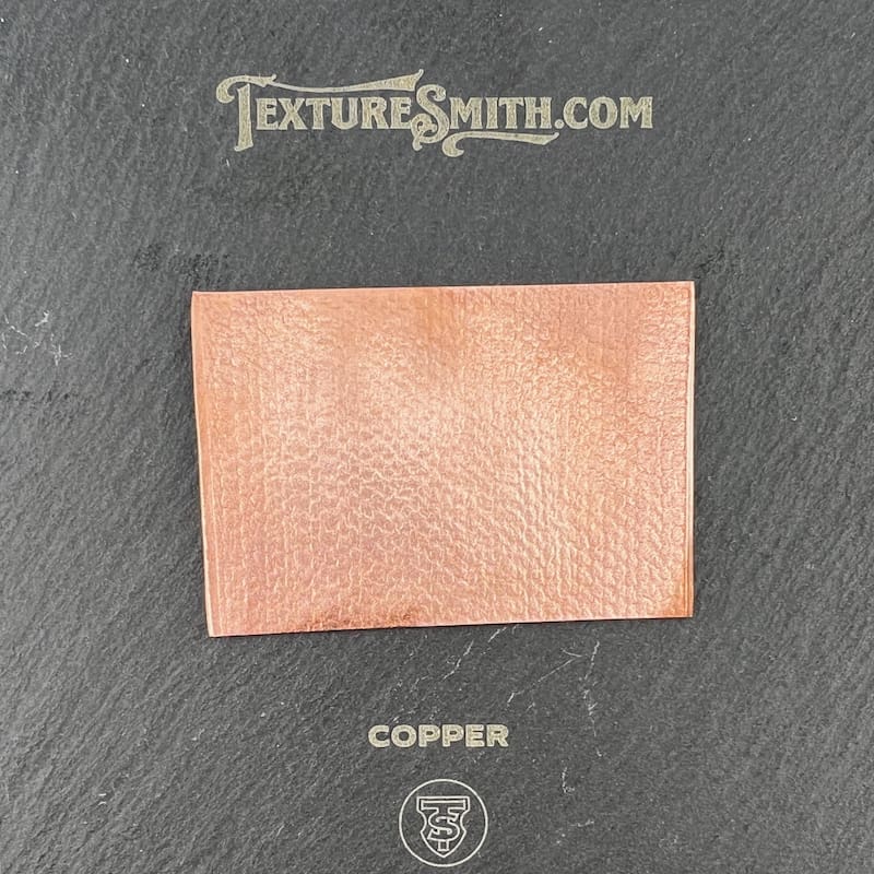 A textured copper sheet with a subtle pattern on a dark background.