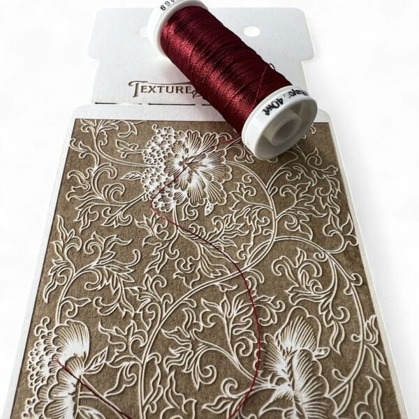 Intricate floral embroidery pattern with a spool of deep red thread.