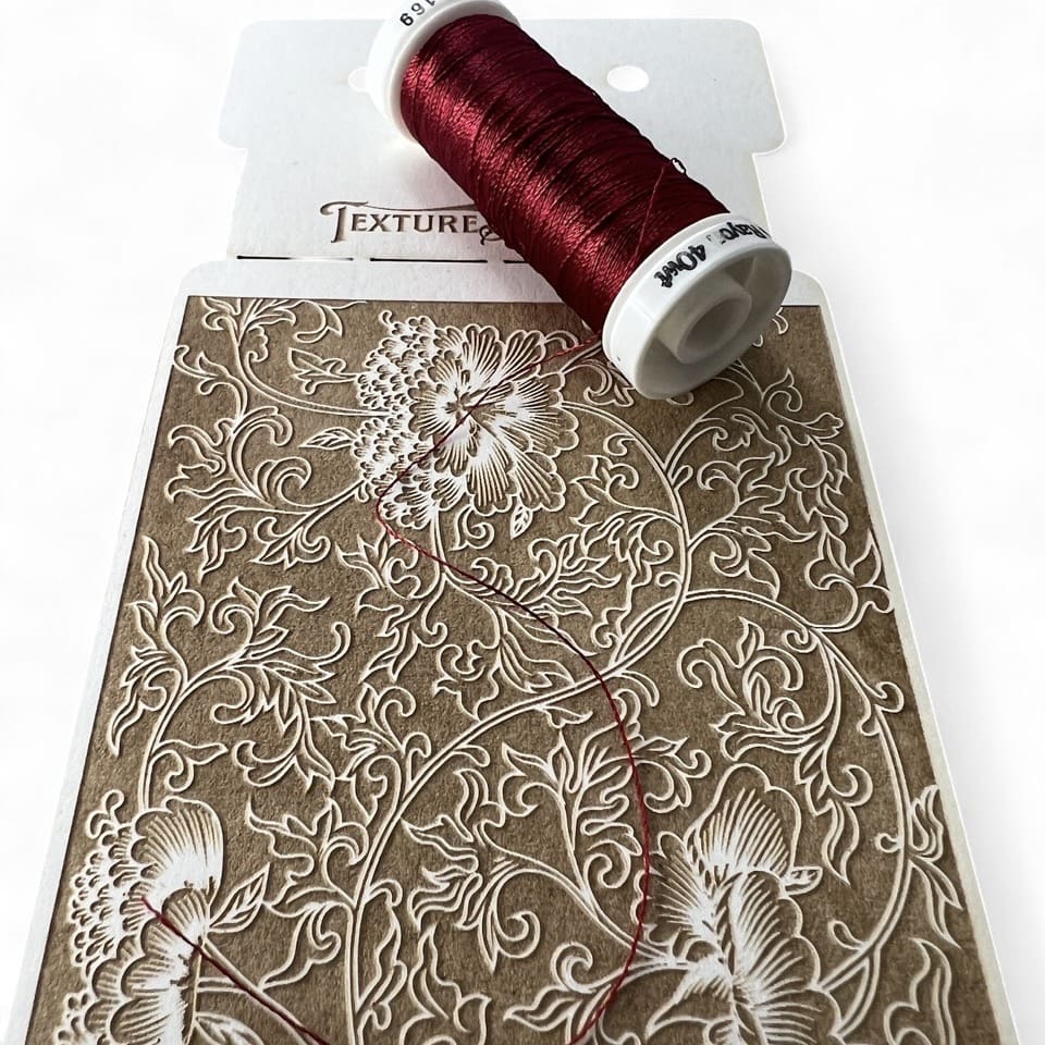 Intricate floral embroidery pattern with a spool of deep red thread.