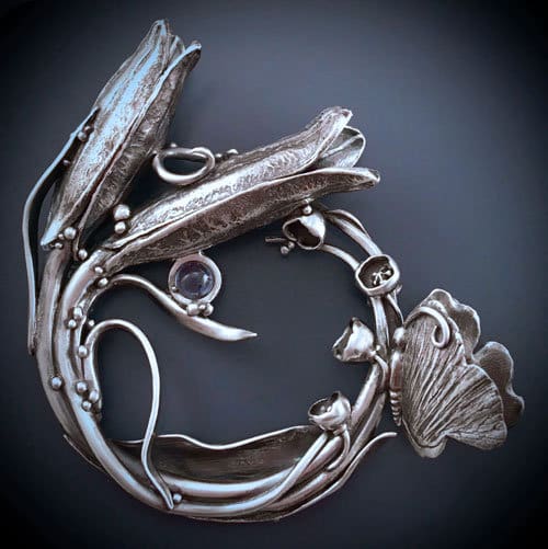 Intricate silver jewelry piece with floral and scroll motifs.